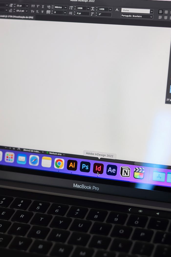 A detailed view of a MacBook Pro displaying Adobe InDesign and other design tools on screen.