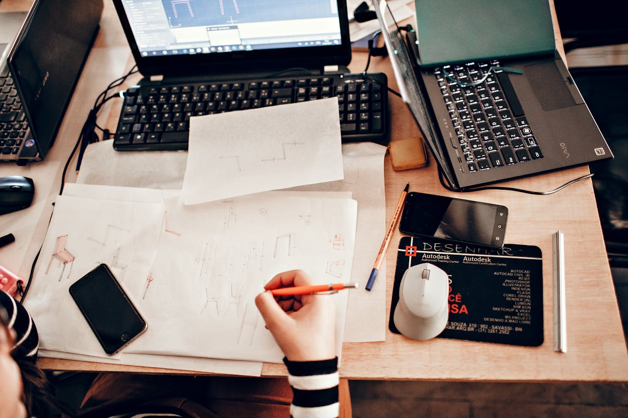 Top view of a business workspace with sketches, laptops, and drawing tools.